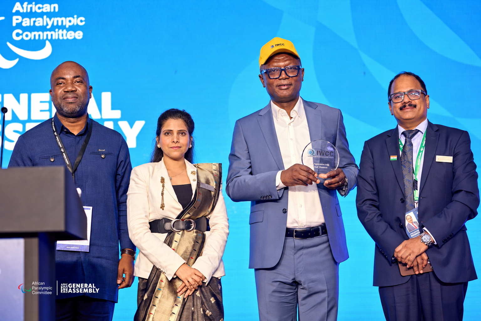 Four guests pose on stage, with an IWCC-marked award held by the central participant.
