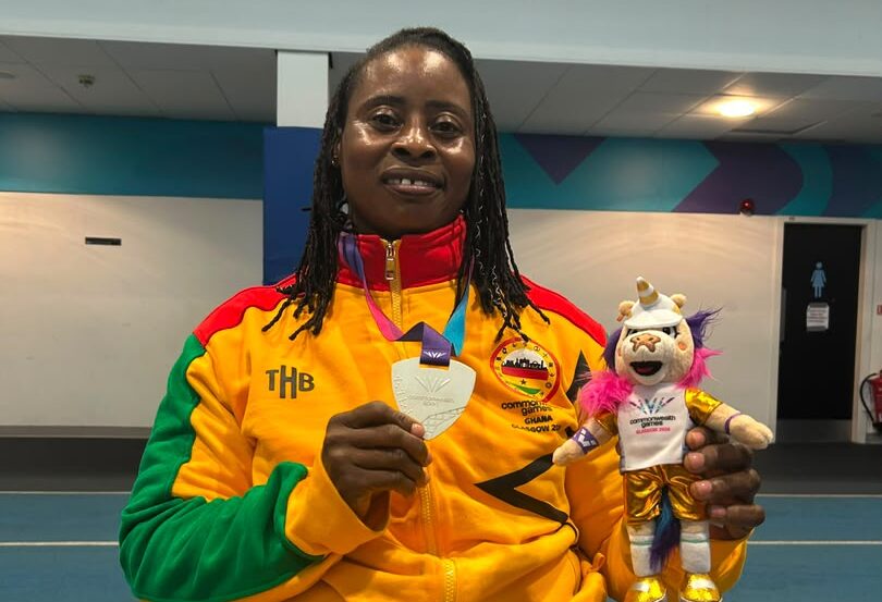 Zinabu Issah, wearing Ghana team colours, holds a medal and a Games mascot.