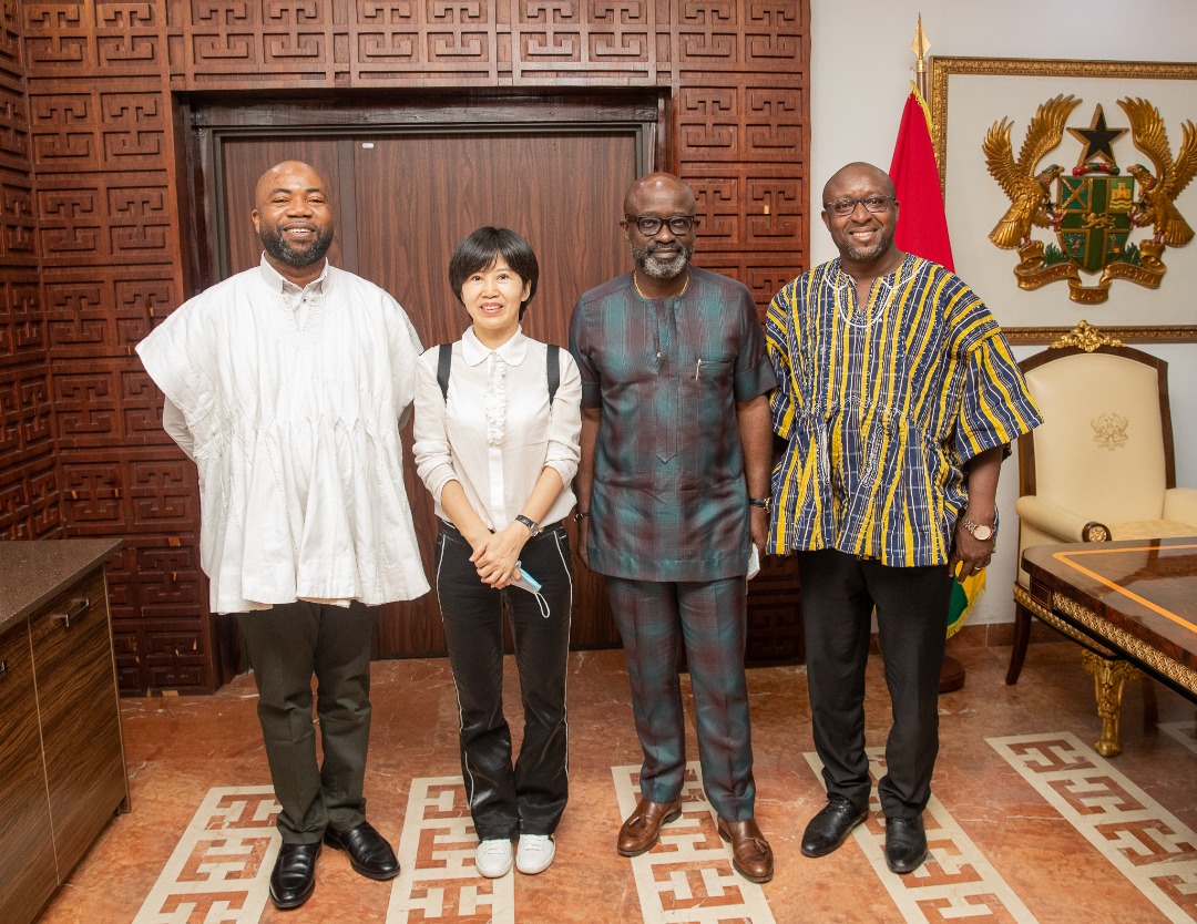 Four delegation members pose beside the Ghana coat of arms.