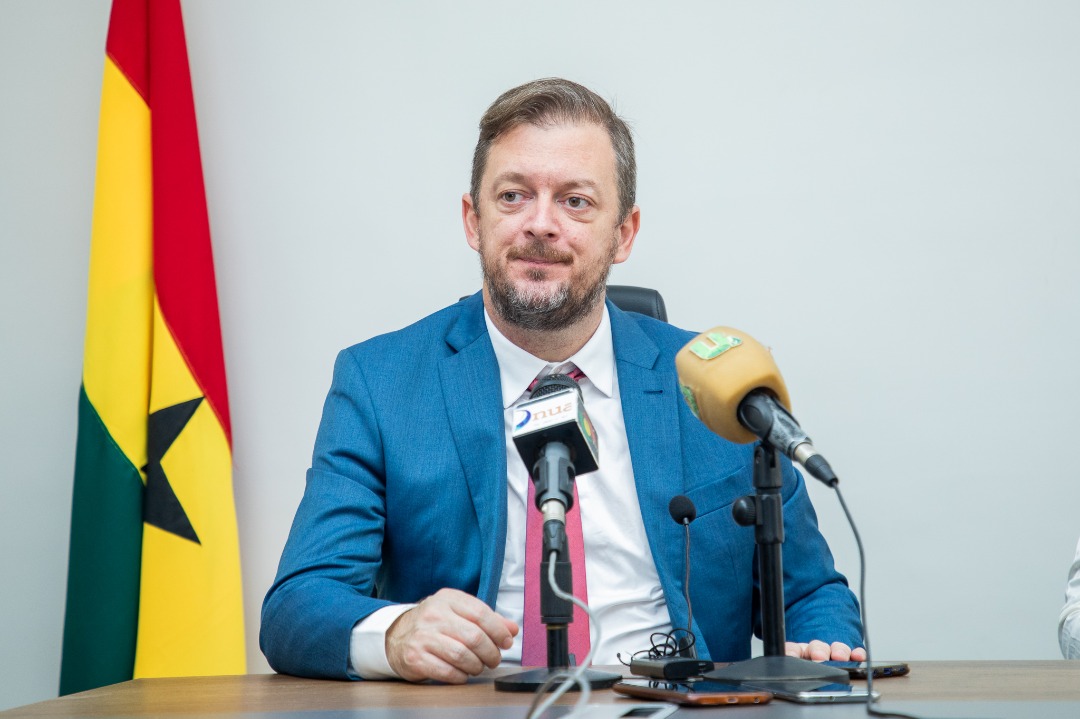 Andrew Parsons seated at the media table with the Ghana flag behind him.